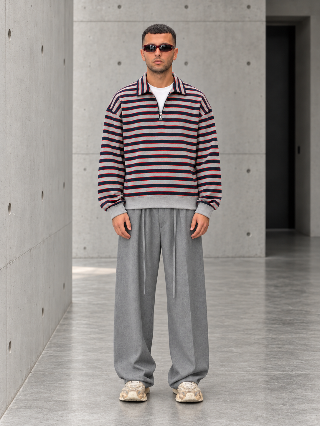 Outfit con polo a righe e pantalone grigio sul cemento